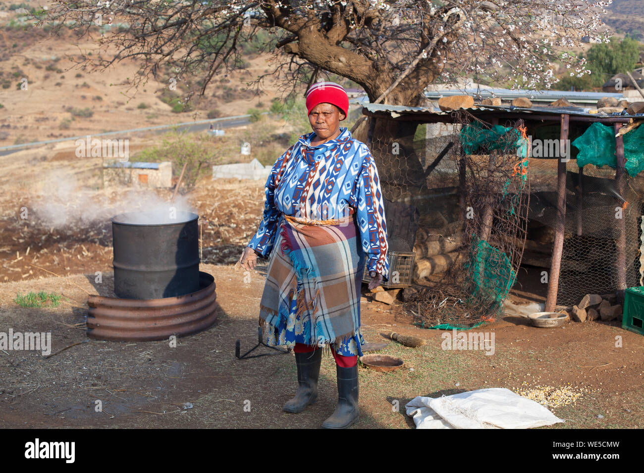 Ramabanta, Lesotho - 20 septembre 2017 : african woman in traditional couverture vêtements brews boisson nationale en fût métallique, village courtyard, Afrique Banque D'Images