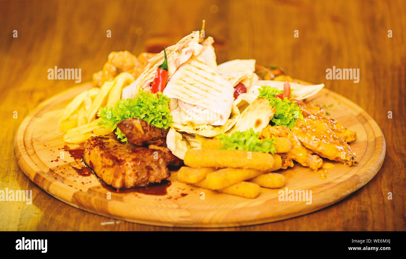 Planche de bois avec beaucoup de frites et bâtonnets de poisson viande burrito steak servi avec une salade. Menu snack-bar. Calories élevé pour le groupe d'amis. De délicieux en-cas savoureux. Les repas au restaurant. Snack pour la bière. Banque D'Images
