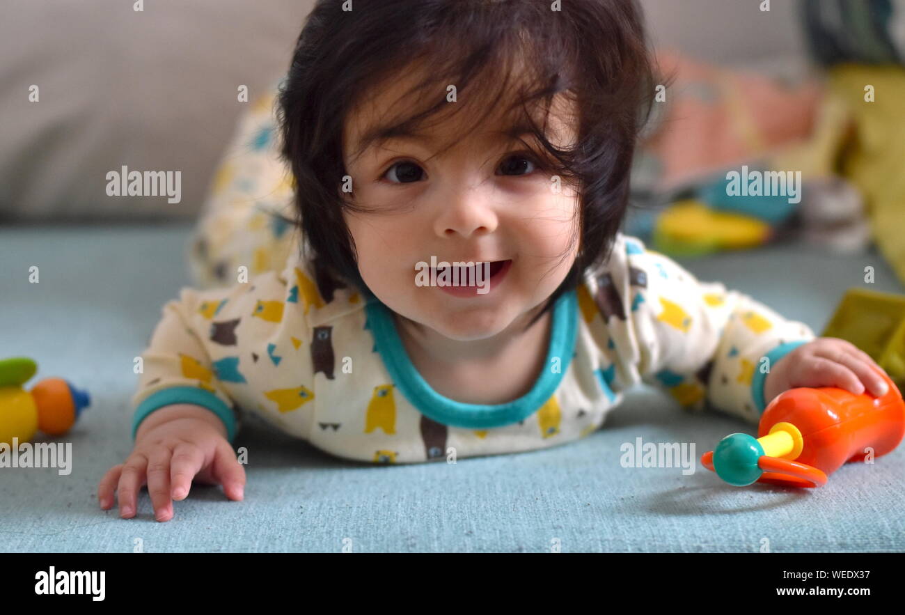 Cute baby smiling at camera entouré par des jouets couchée sur son ventre Banque D'Images
