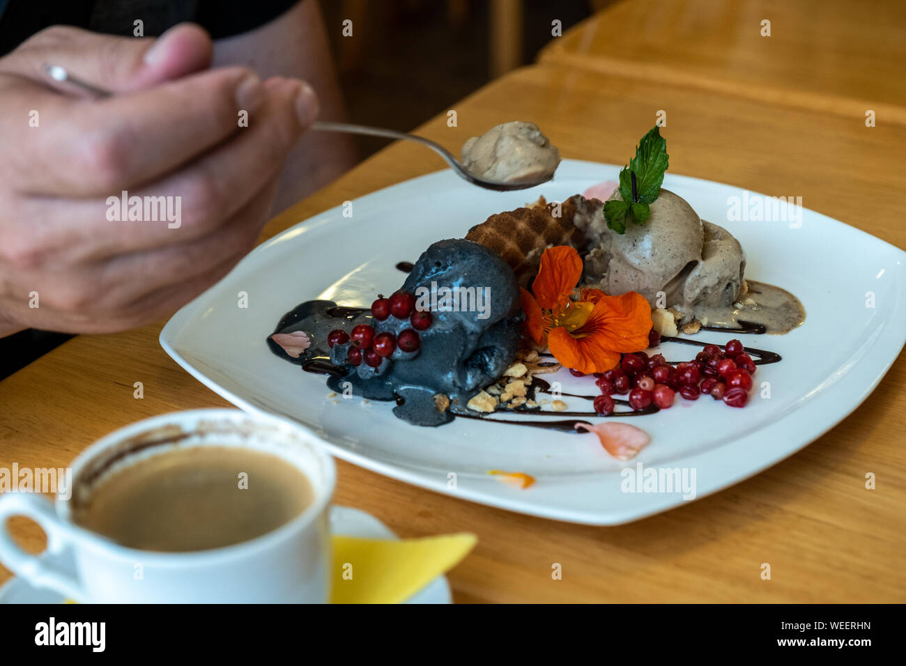 Un homme mange du charbon et de la chicorée la crème glacée, décoré avec des gaufres et de baies fraîches. Banque D'Images