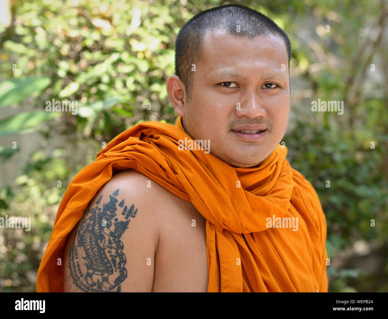 Jeune moine bouddhiste thaï avec un tatouage sur son bras supérieur droit sourire pour la caméra. Banque D'Images