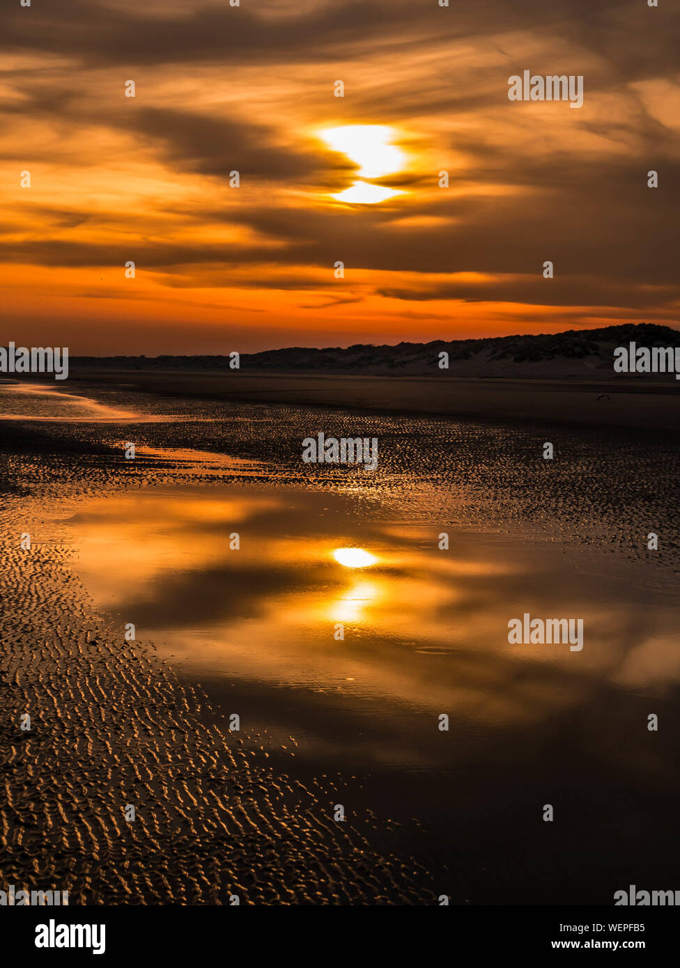 Coucher de soleil coloré avec furtivement à travers les nuages et le sable ondulations dans l'avant-plan à marée basse Banque D'Images