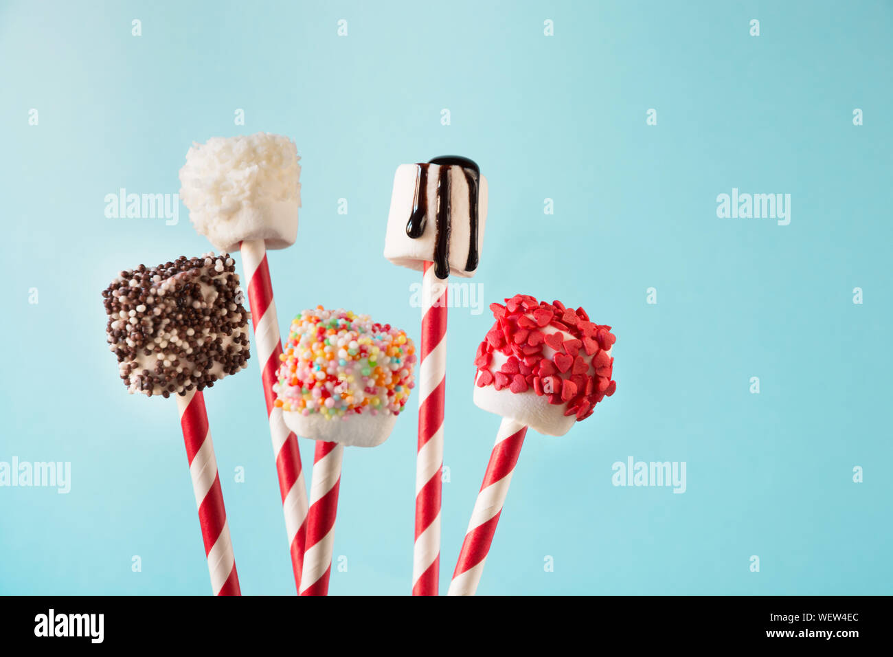 Sweet moelleux marshmallow et sucettes sur paille décoré avec du chocolat fondu et des gâteaux Sprinkles sur fond bleu. Les enfants adoreront ces décisions. Cop Banque D'Images