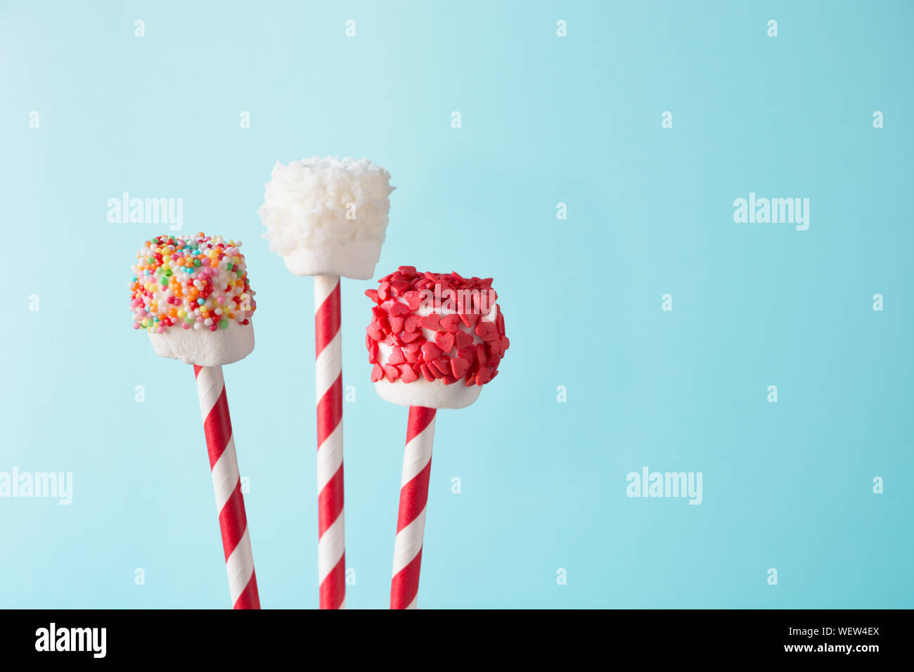 Sweet moelleux marshmallow et sucettes sur paille décoré avec du chocolat fondu et des gâteaux Sprinkles sur fond bleu. Les enfants adoreront ces décisions. Cop Banque D'Images