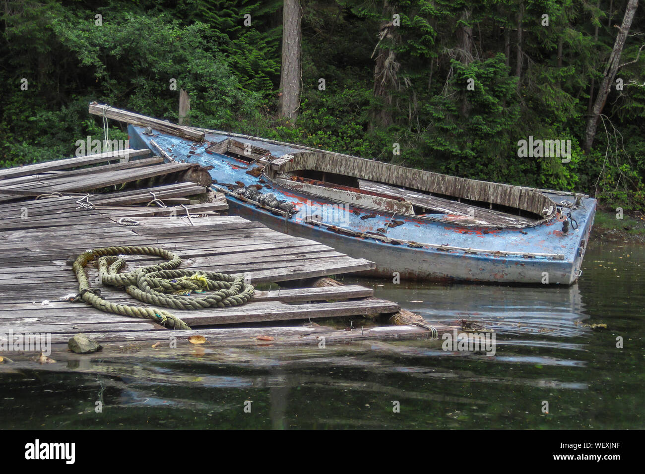 Une épave, dépouillé vieille or dayboat se trouve dans les eaux peu profondes à un dock délabré sur une rive boisée dans un coin tranquille sur la côte de la Colombie-Britannique. Banque D'Images