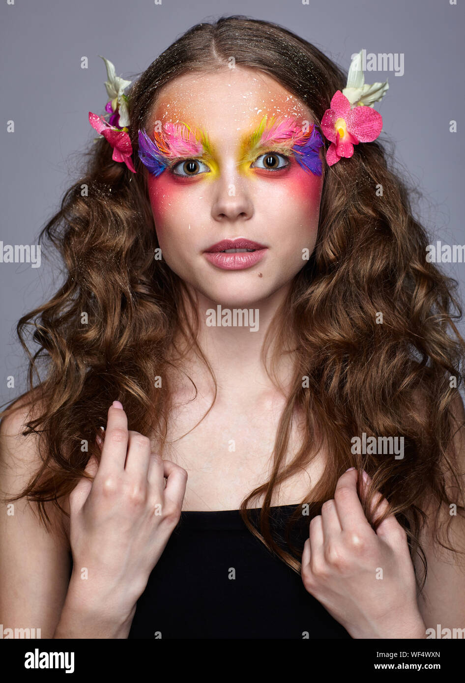 Portrait de jeune fille avec orchidée, fleur dans les cheveux ondulés à la caméra dans l'expression d'émerveillement. Jeune femme avec une rare élégance et a de faux fa Banque D'Images
