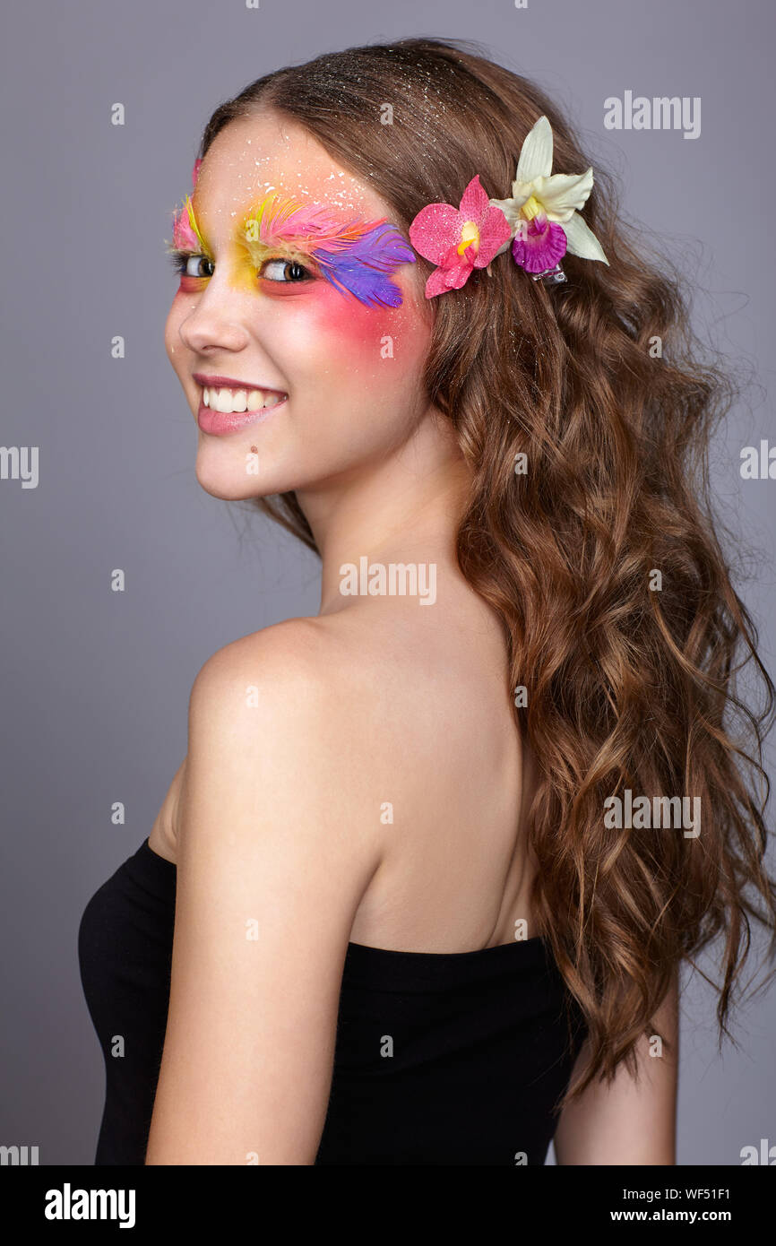 Portrait of happy smiling teen girl. Jeune femme avec une rare élégance et de faux cils en plumes de la mode. Orchidée, fleur dans les cheveux ondulés. Banque D'Images