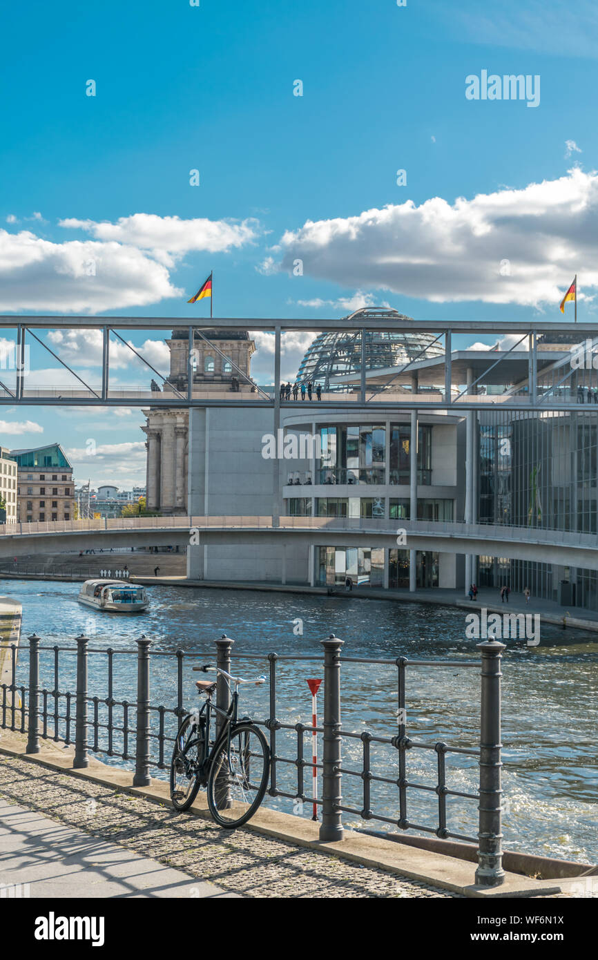 Vue panoramique d'une bicyclette se penchant dans une clôture métallique, avec un bateau école sur la rivière Spree et à l'architecture métallique du parlement allemand avec nati Banque D'Images
