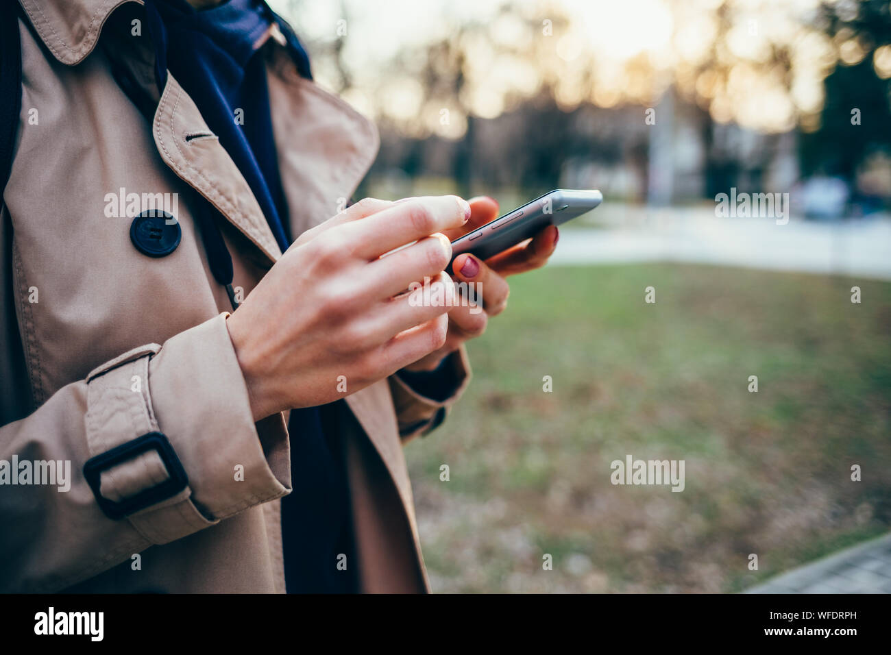Femme dans un manteau beige est titulaire d'un téléphone mobile dans ses mains dans le parc Banque D'Images