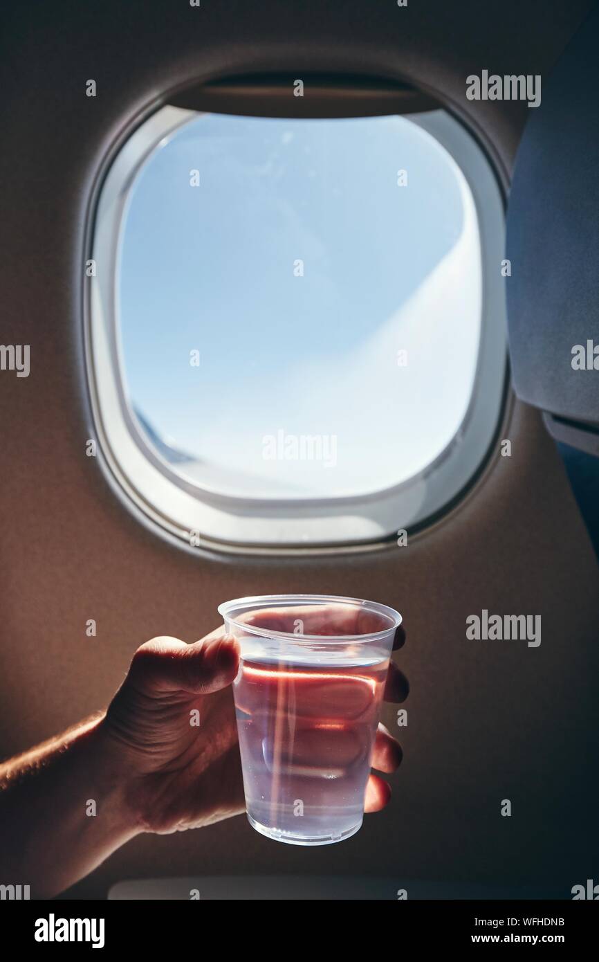 Pendant le vol de rafraîchissement. Human hand holding cup d'eau potable contre la fenêtre de l'avion. Banque D'Images
