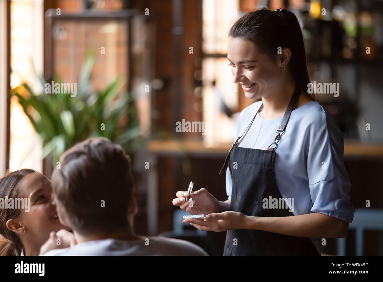 Smiling female waitress prendre commande couple parler aux clients Banque D'Images