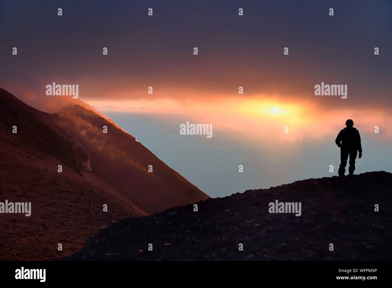 Italie, Sicile, Îles Éoliennes, classé au Patrimoine Mondial de l'UNESCO, l'île de Stromboli, randonneur regardant les fumerolles d'une éruption sur les pentes du volcan actif au coucher du soleil Banque D'Images