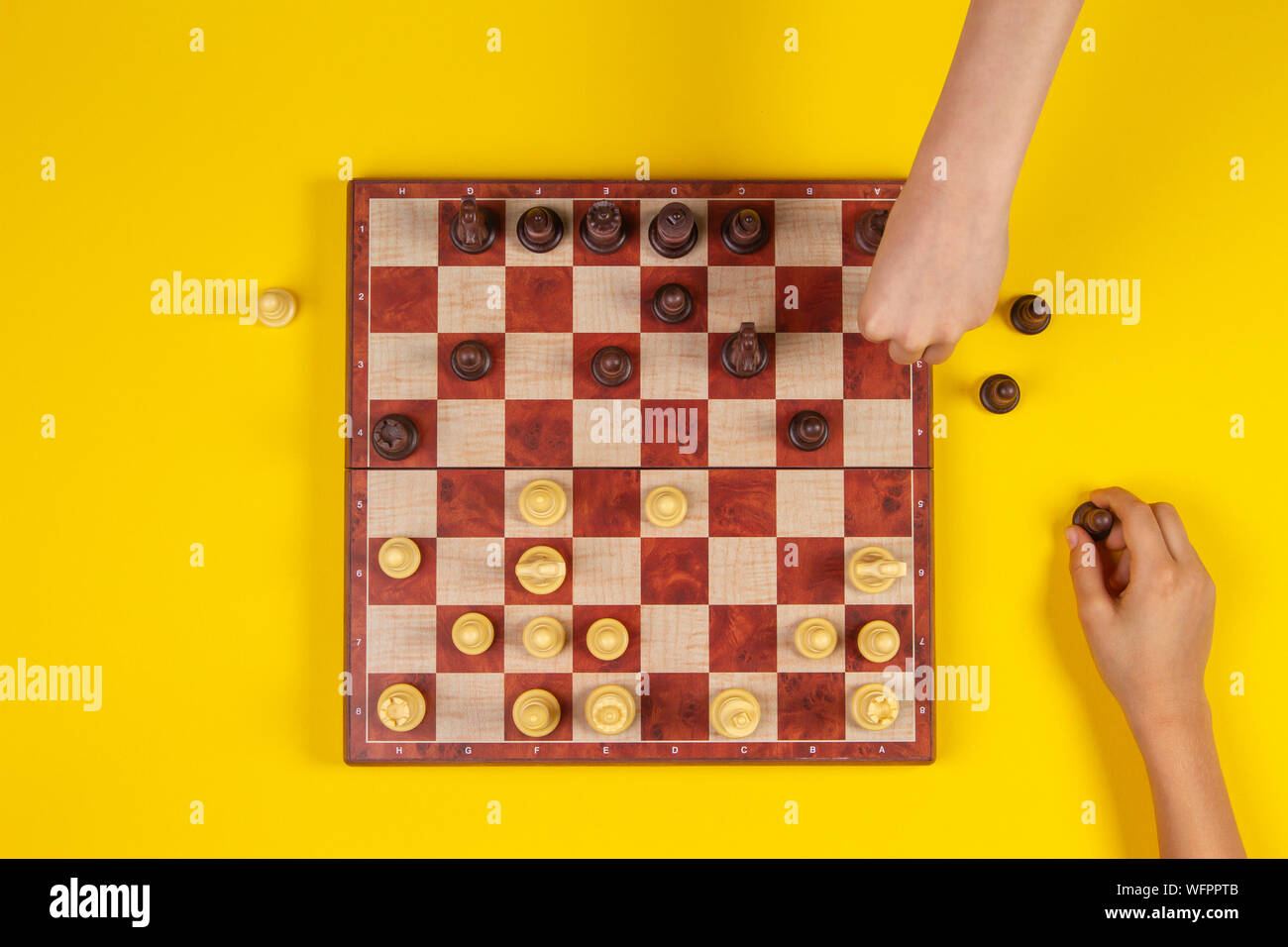 Les enfants les mains sur un échiquier jouant aux échecs sur fond jaune, vue du dessus Banque D'Images