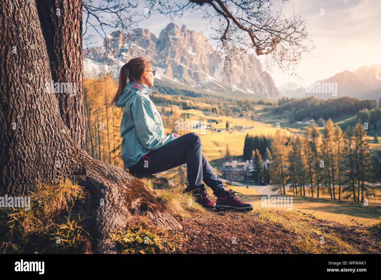 La femme est assise sur la colline sous l'arbre à coucher de soleil en automne Banque D'Images