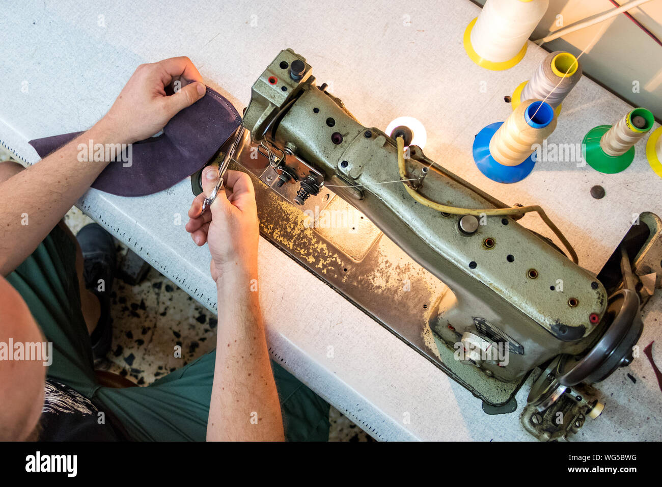Vue de dessus d'un mâle shoemaker couper un thread après coudre le cuir avec une vieille machine à coudre. Banque D'Images