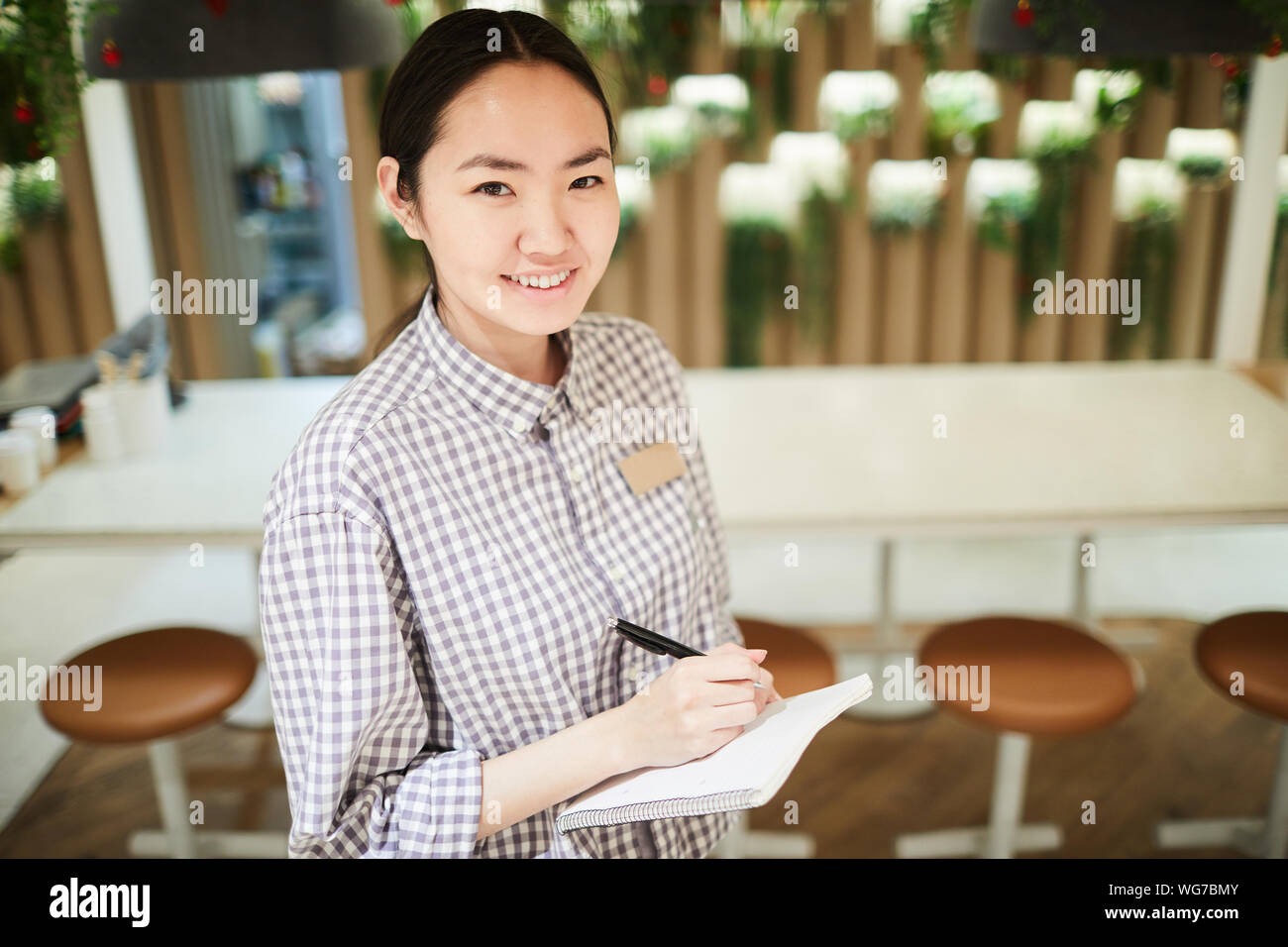 High angle portrait of smiling waitress looking at camera pendant la prise de vue en cafe, copy space Banque D'Images