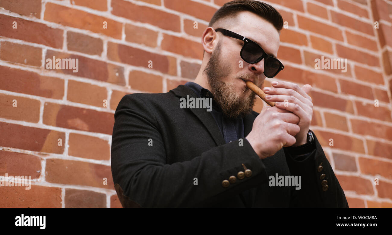 Vue de dessous du côté beau barbu fumant un cigare sur mur de brique Banque D'Images