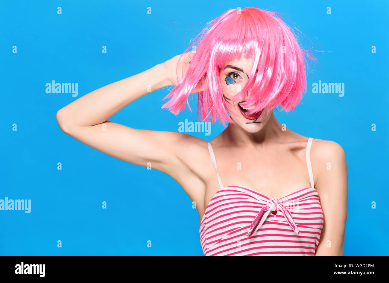 Head shot de beauté. Jeune femme avec pop art créatif maquillage et perruque rose regardant la caméra sur fond bleu. Banque D'Images