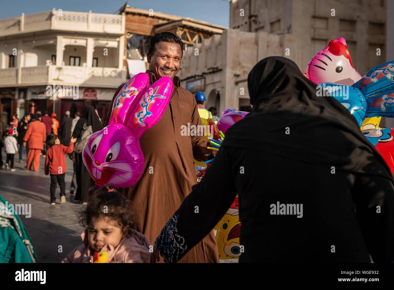 Doha, Qatar - 17 déc 2016 : Un homme vendeur de rue est à la recherche à l'appareil photo et la vente d'un ballon coloré pour une fille et une femme portant un traditionnel ab Banque D'Images