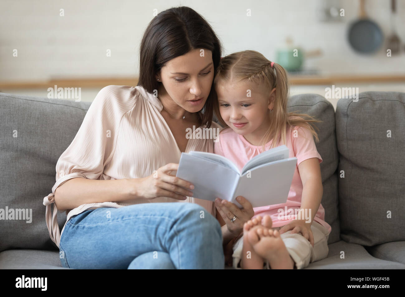 Mother and Daughter sitting on couch reading a book Banque D'Images