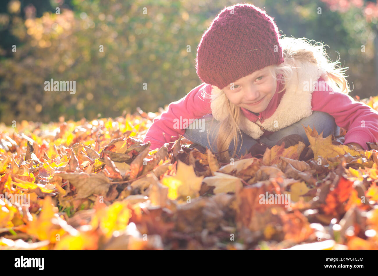 Portrait of smiling girl en atmosphère d'automne colorés assis parmi les feuilles jaunes et orange vif Banque D'Images