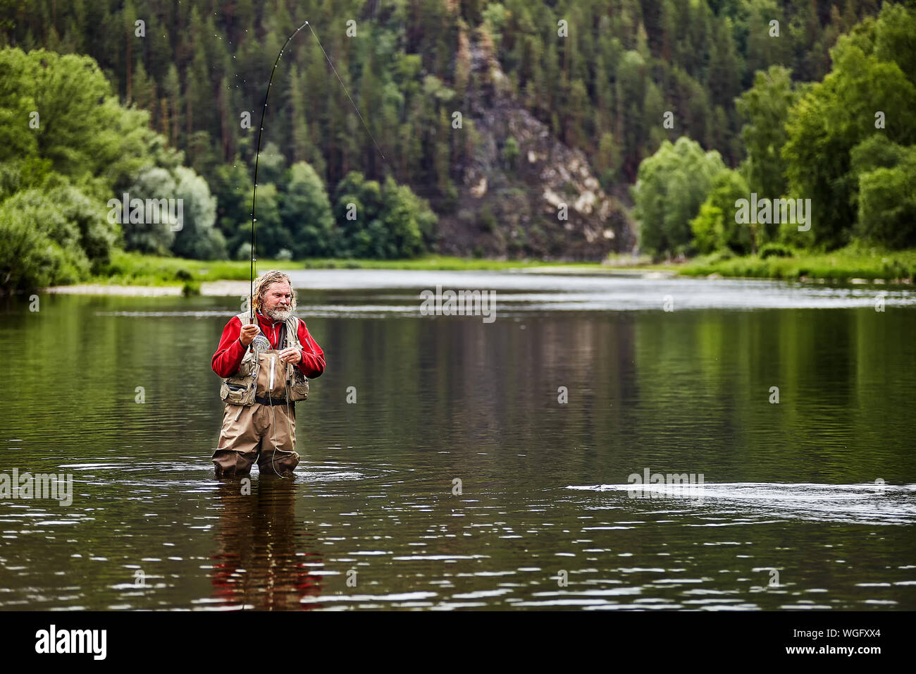 Le pêcheur de poissons captures par pêche à la mouche ou le moulage. Un pêcheur dans l'équipement de pêche étanche s'enfonça dans l'eau de la rivière. Banque D'Images