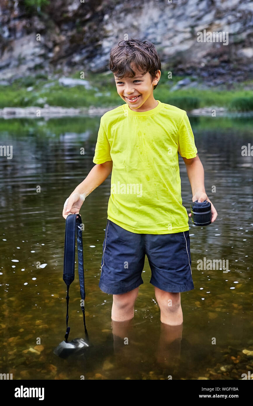 Un enfant joue avec ses pères cher appareil photo. Un joyeux petit garçon enlevé la lentille, d'un appareil photo reflex numérique et abaissé le gadget sous le wat Banque D'Images