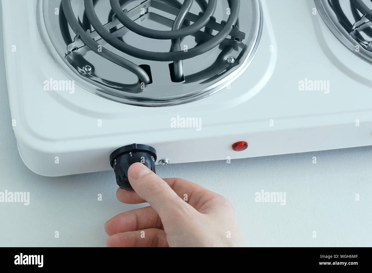 La main de Caucasian girl tourne sur une cuisinière électrique. Close-up. Banque D'Images