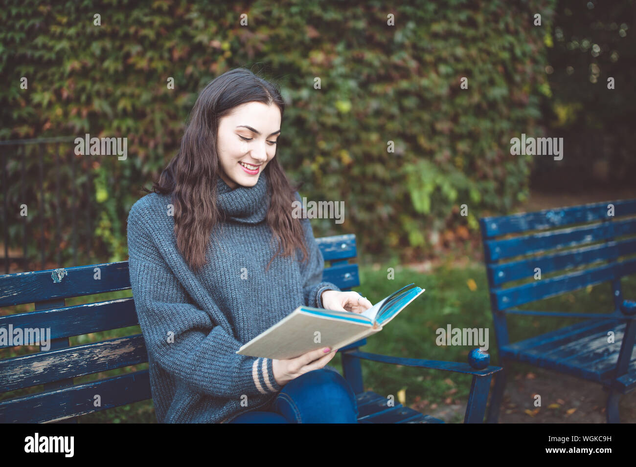 Jeune femme dans un chandail de lire un livre, assis sur le banc dans le parc. Temps d'automne. Banque D'Images