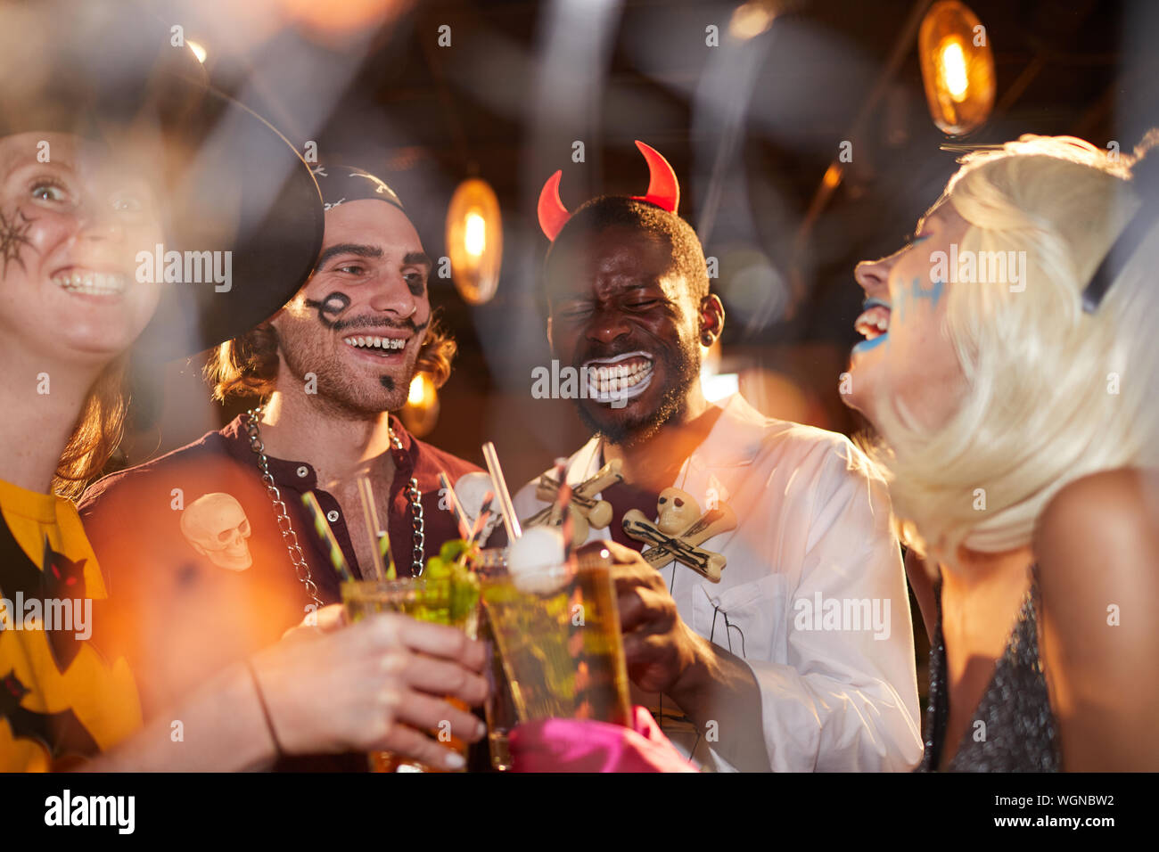 Groupe multiethnique d'amis adultes portant des costumes de Halloween de boire des cocktails tout en profitant de parti au club et avoir du plaisir Banque D'Images