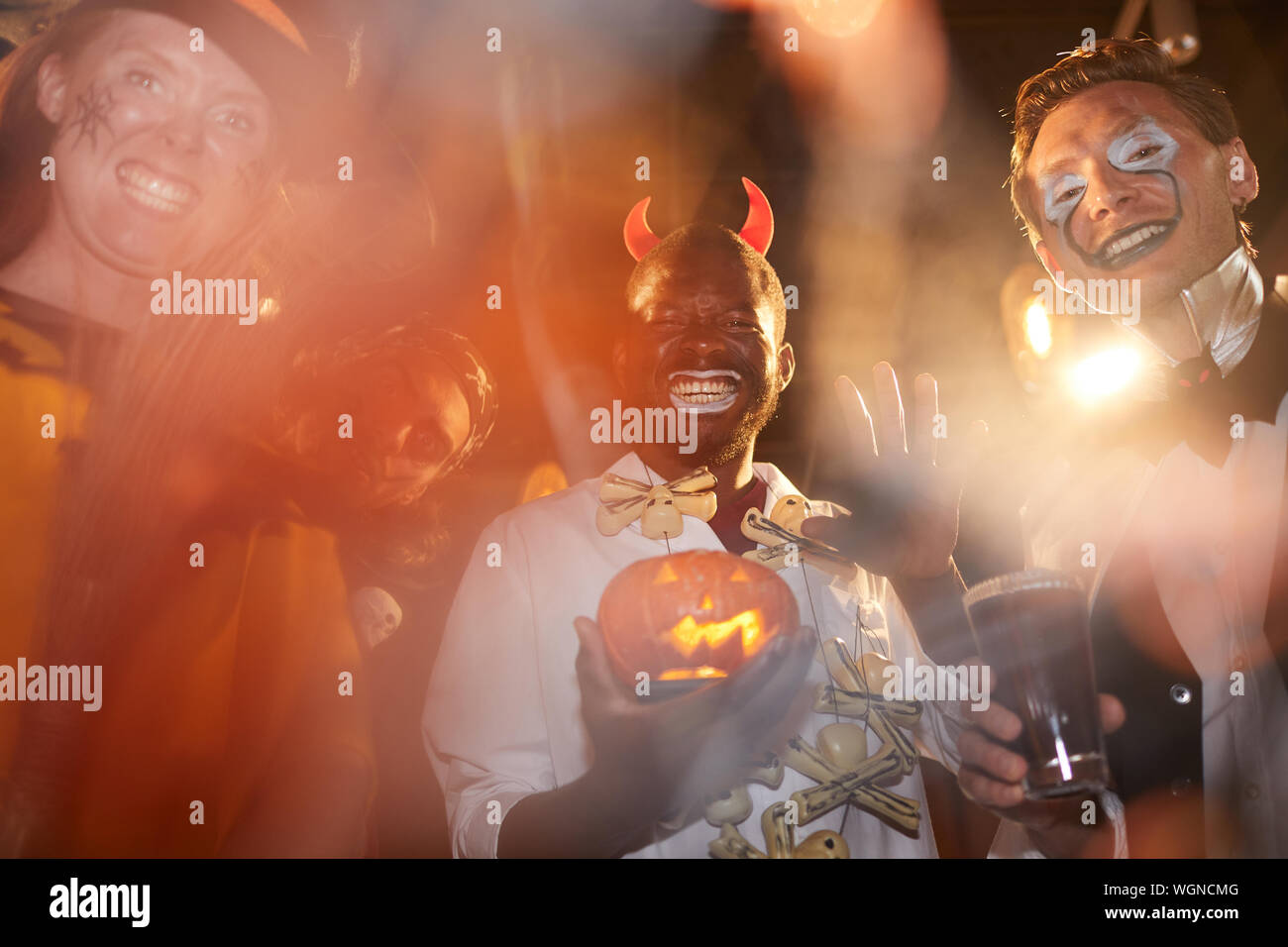 Low angle view au groupe des adultes hommes portant des costumes de Halloween posant au cours de partie en club, se concentrer sur l'homme afro-américain holding pumpkin dans le centre Banque D'Images