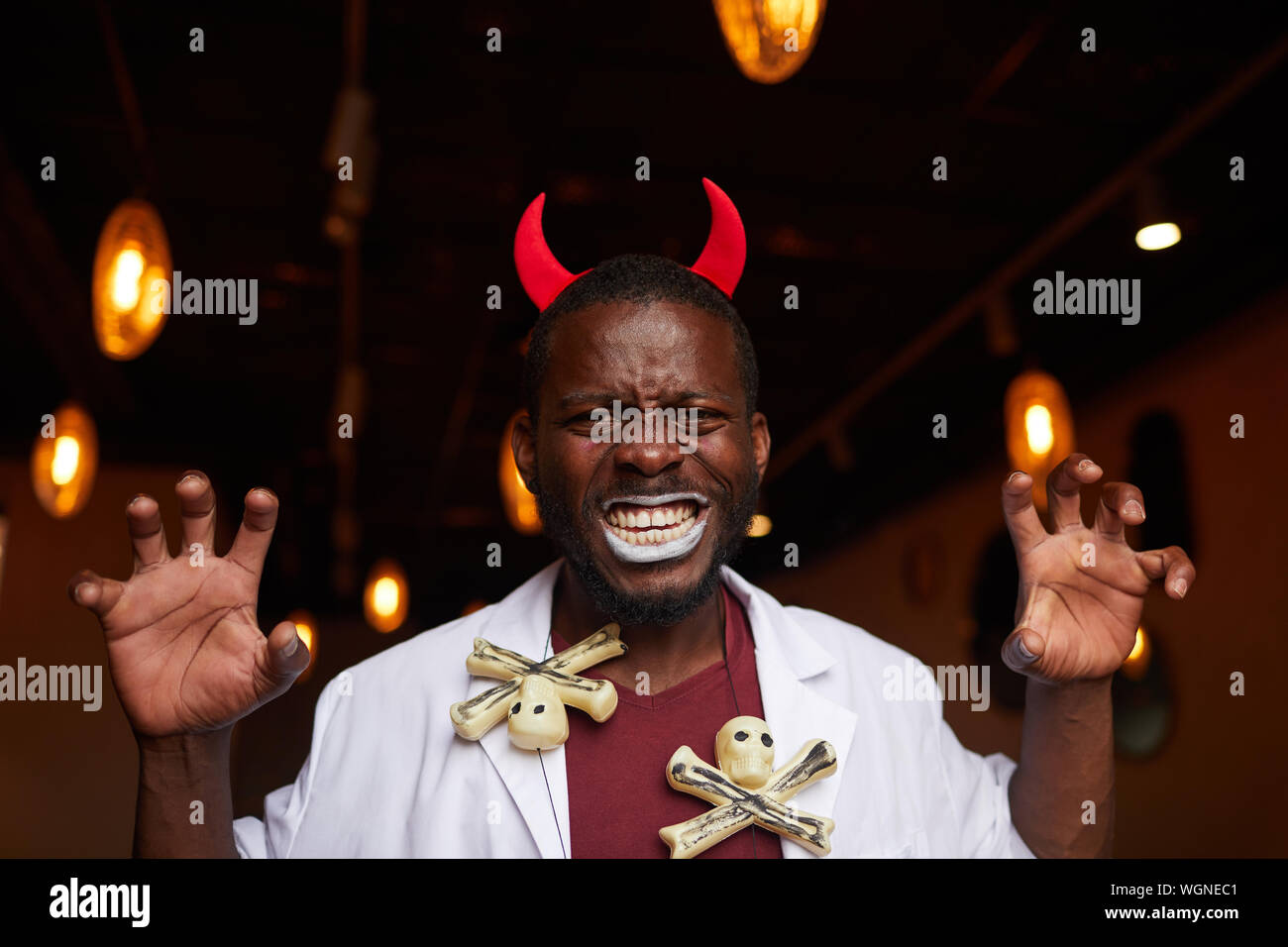 Portrait de l'homme afro-américain adultes portant des cornes de diable grimaçant se faisant passer à huis clos pendant Halloween party in nightclub, copy space Banque D'Images