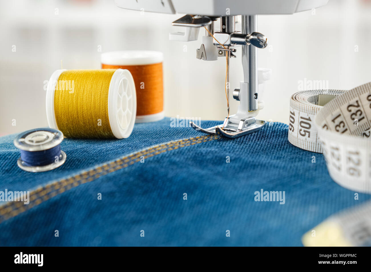 Jeans couture avec machine à coudre. Close up de l'aiguille de machine à coudre sur le tissu denim stitch, bobines de fils et ruban à mesurer. Banque D'Images
