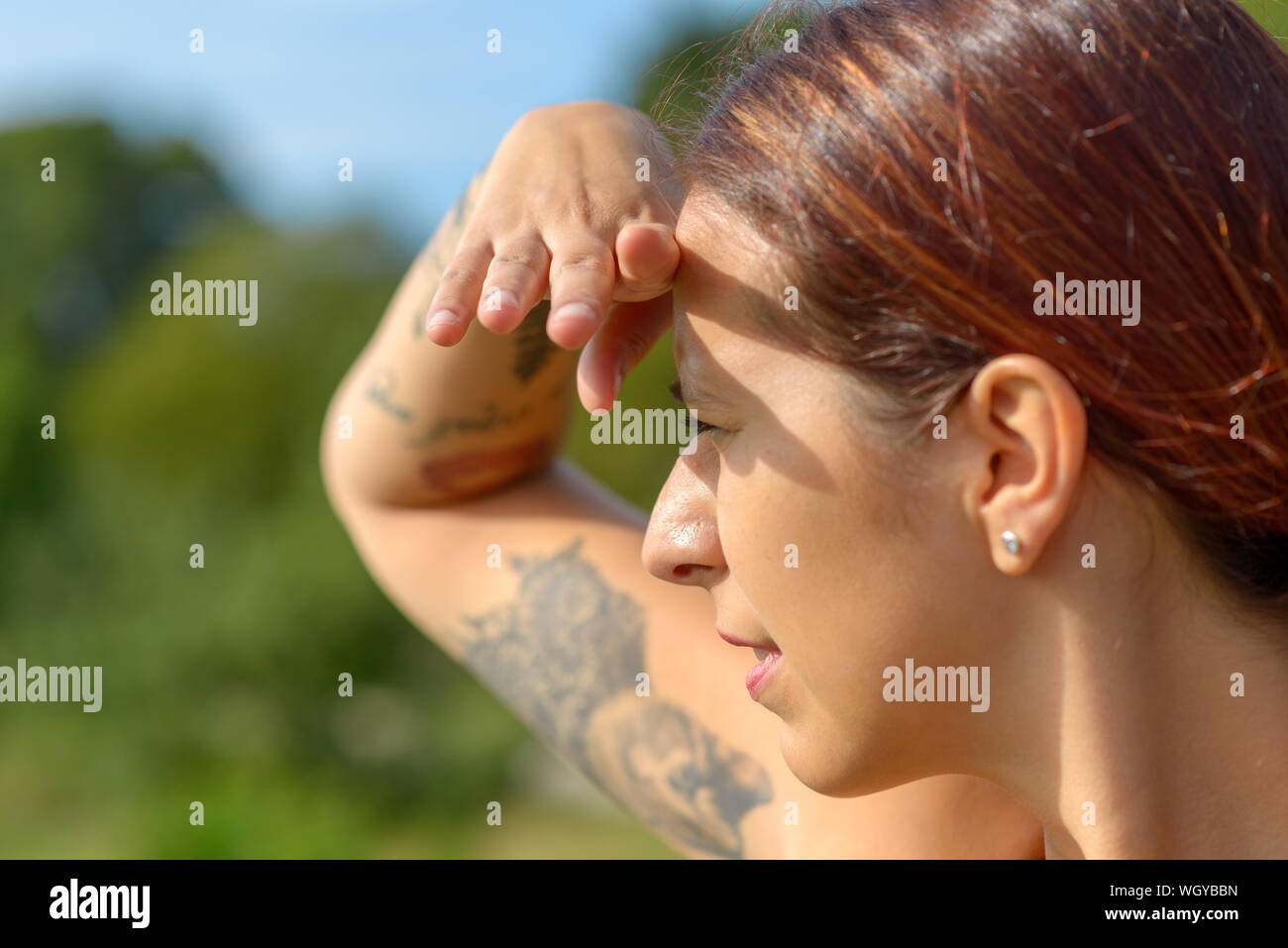 Jolie femme gardant un oeil dehors avec sa main posée sur son front pour protéger ses yeux du soleil et un sourire heureux Banque D'Images