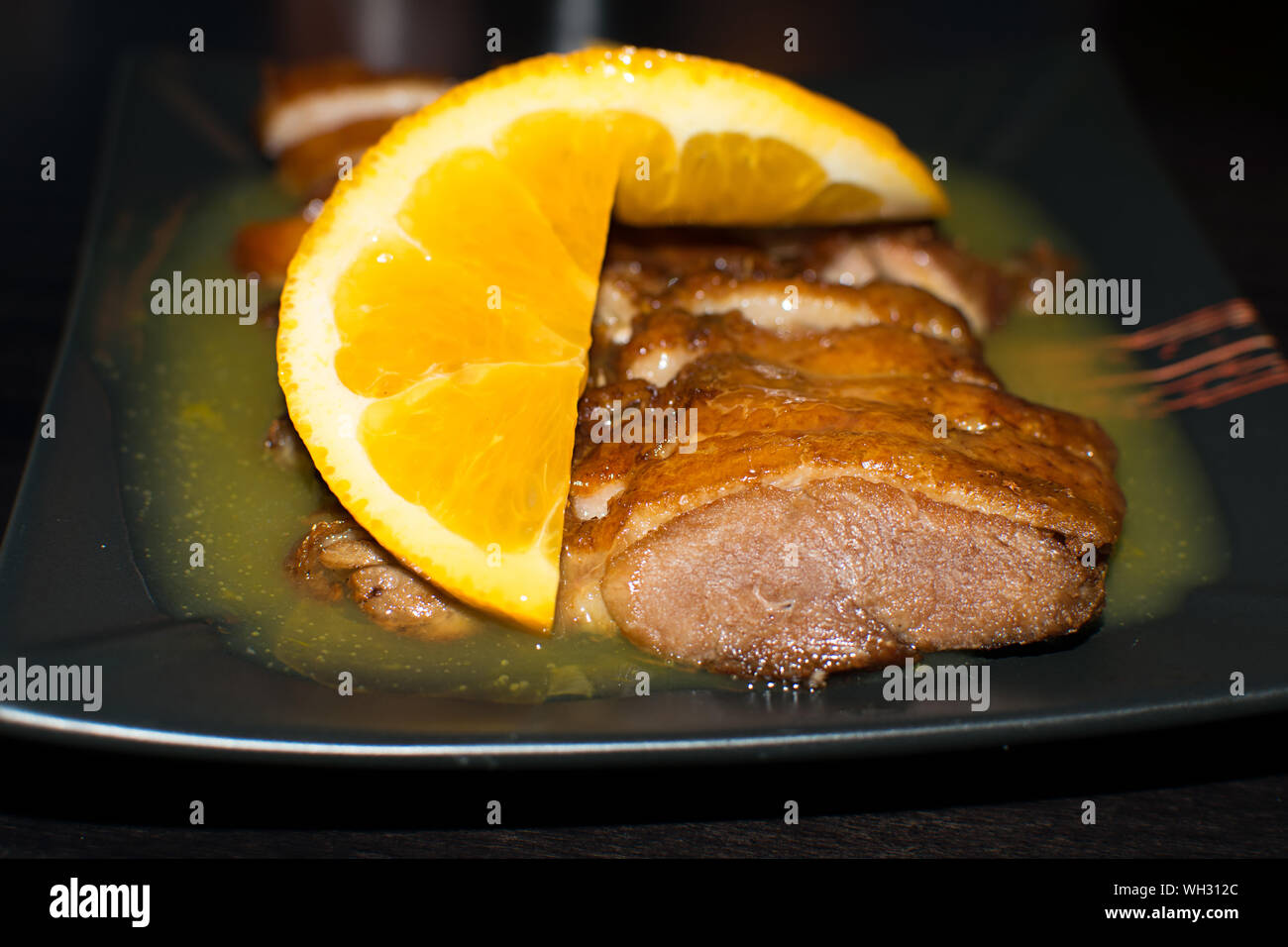 Photo en gros plan de le canard rôti servi avec sauce à l'orange et les tranches sur une assiette noire. Recette chinoise d'Orange duck. Espagne, 2019. Banque D'Images