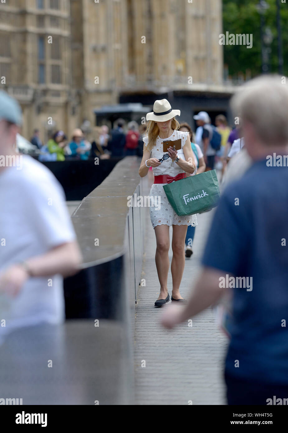 Londres, Angleterre, Royaume-Uni. Woman son téléphone à l'extérieur du Parlement, portant un sac de Fenwick. Banque D'Images