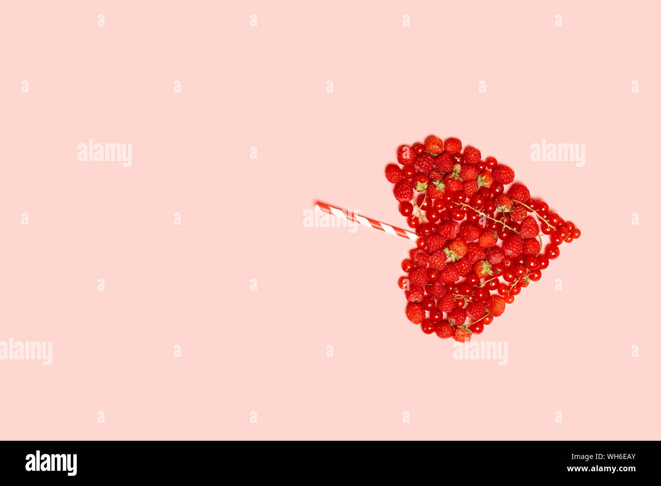 Un assortiment de fruits rouges mûrs de framboises, groseilles et fraises avec un cocktail du bar rayé paille sur fond rose. Concept de l'alimentation d'été Banque D'Images