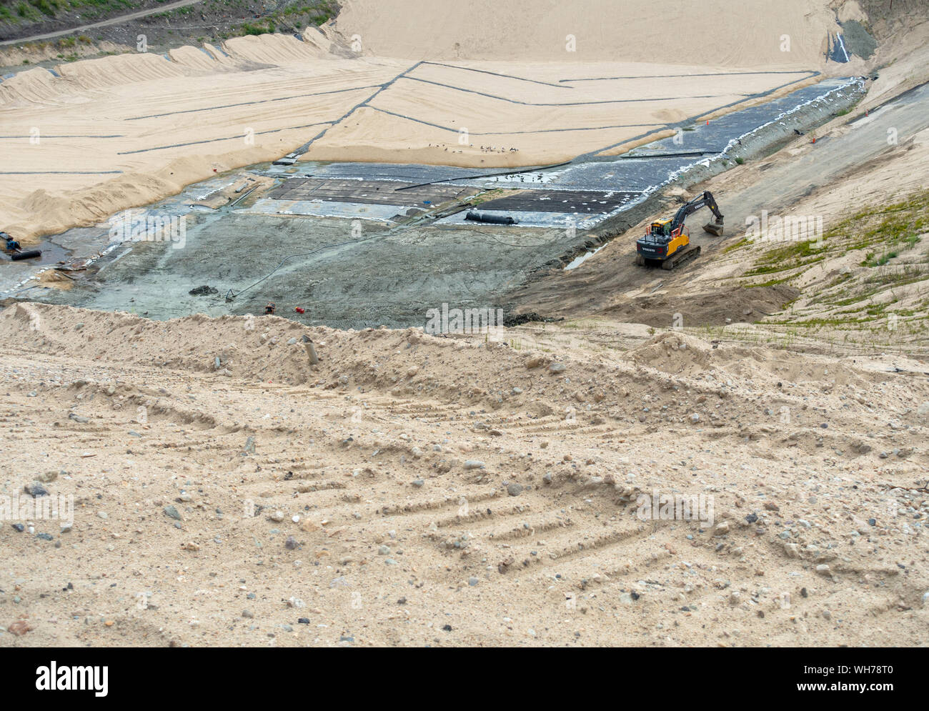 Une pelleteuse se trouve au bas de l'enfouissement en construction site d'immersion, de cellules d'argile géosynthétique est installé et recouvert de sable Banque D'Images