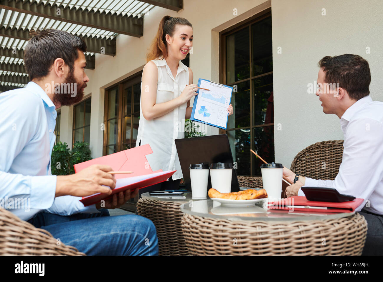 Les jeunes excités businesswoman pointing at graphique dans ses mains et de dire à ses collègues au sujet des progrès de l'entreprise Banque D'Images