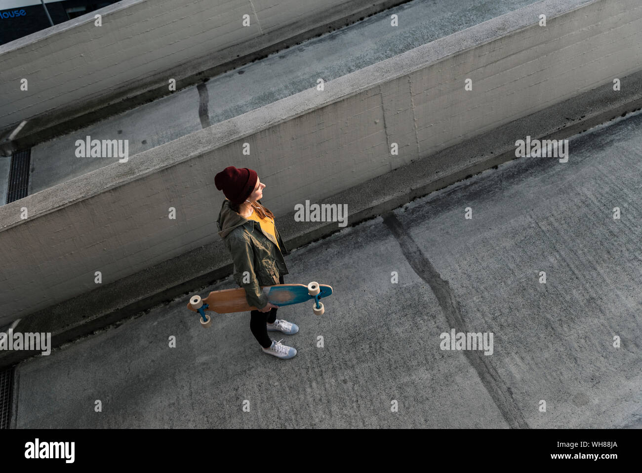 Jeune femme élégante avec skateboard debout sur parking Banque D'Images