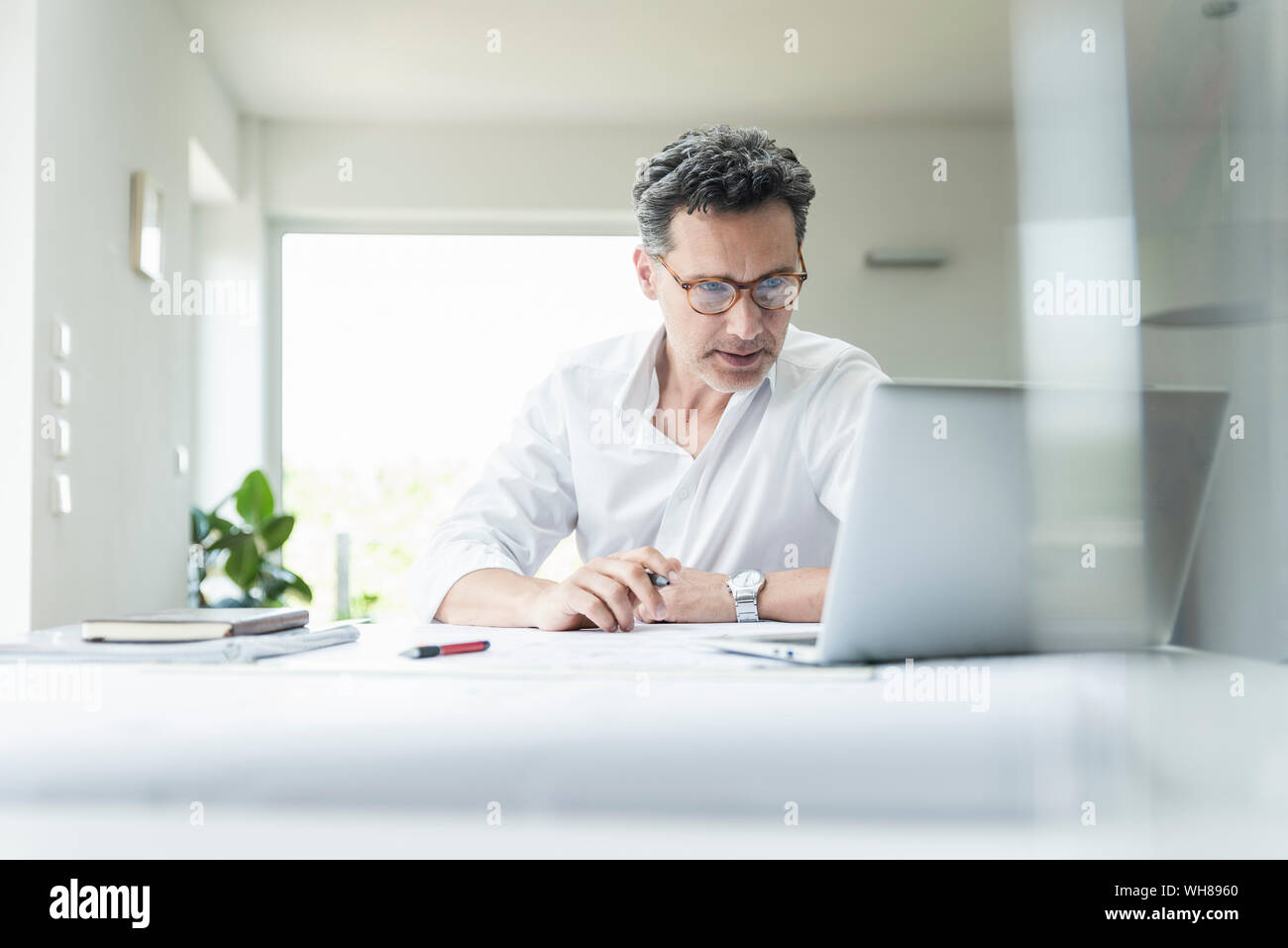 Assis dans le bureau de l'architecte lumineux, using laptop Banque D'Images