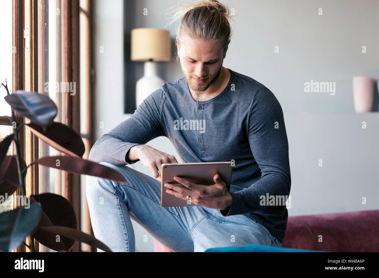 Jeune homme à la maison à l'aide d'une tablette numérique Banque D'Images