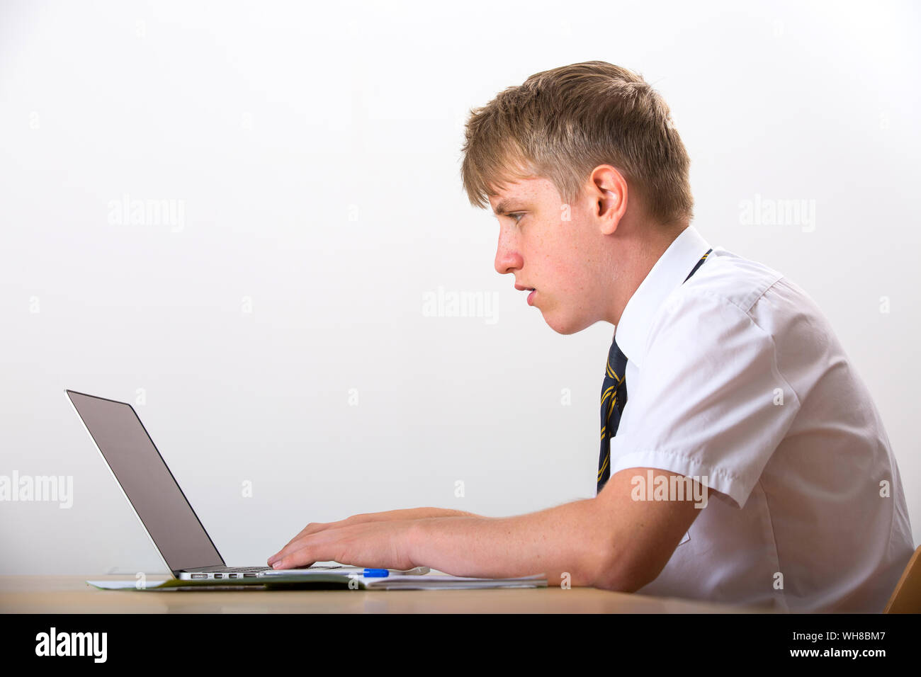 Un jeune garçon en uniforme travaillant sur un ordinateur portable Banque D'Images