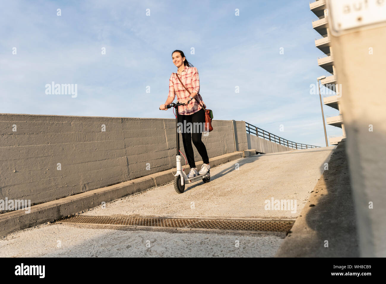 Young woman riding scooter électrique sur le pont-garage Banque D'Images