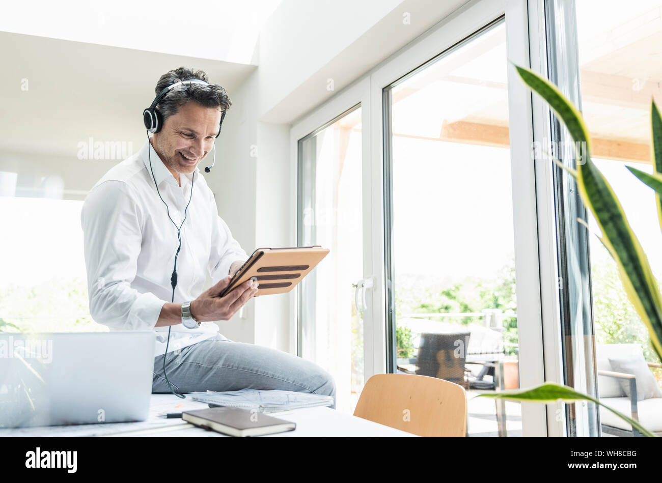 Businessman in bright office avoir conférence téléphonique, à l'aide du casque et digital tablet Banque D'Images