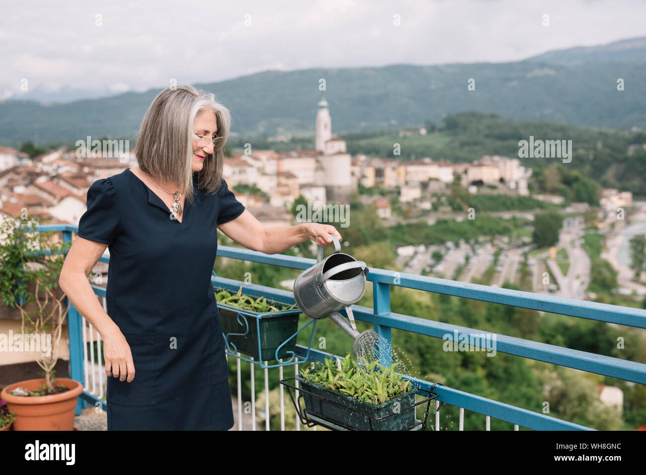 Smiling senior woman watering plants sur son toit-terrasse, Padova, Italie Banque D'Images
