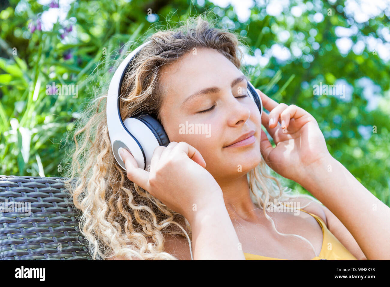 Smiling woman listening to music avec les yeux fermés, allongé sur un transat Banque D'Images