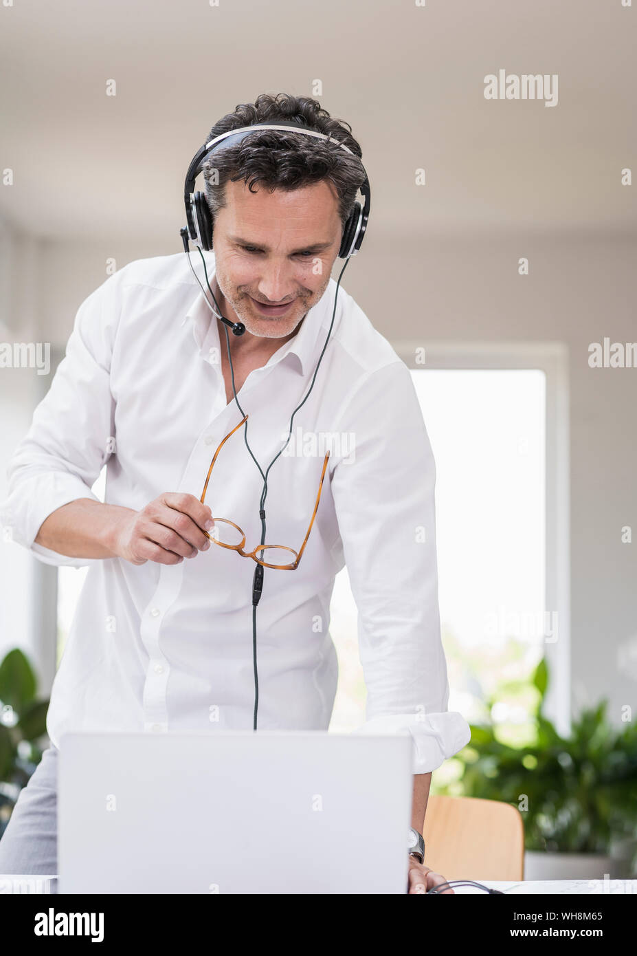 Businessman in bright office avoir conférence téléphonique, à l'aide du casque et l'ordinateur portable Banque D'Images