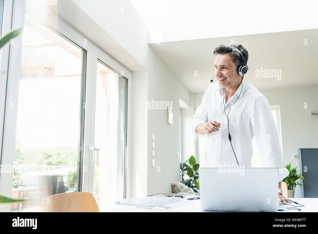 Businessman in bright office avoir conférence téléphonique, à l'aide du casque et l'ordinateur portable Banque D'Images