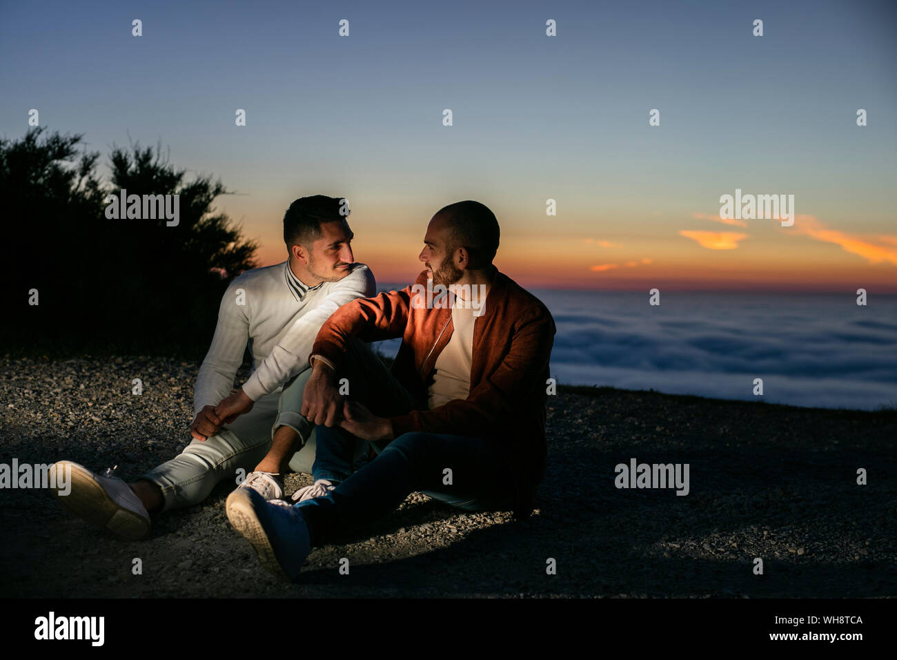 Gay couple assis dans les montagnes au-dessus des nuages au coucher du soleil Banque D'Images